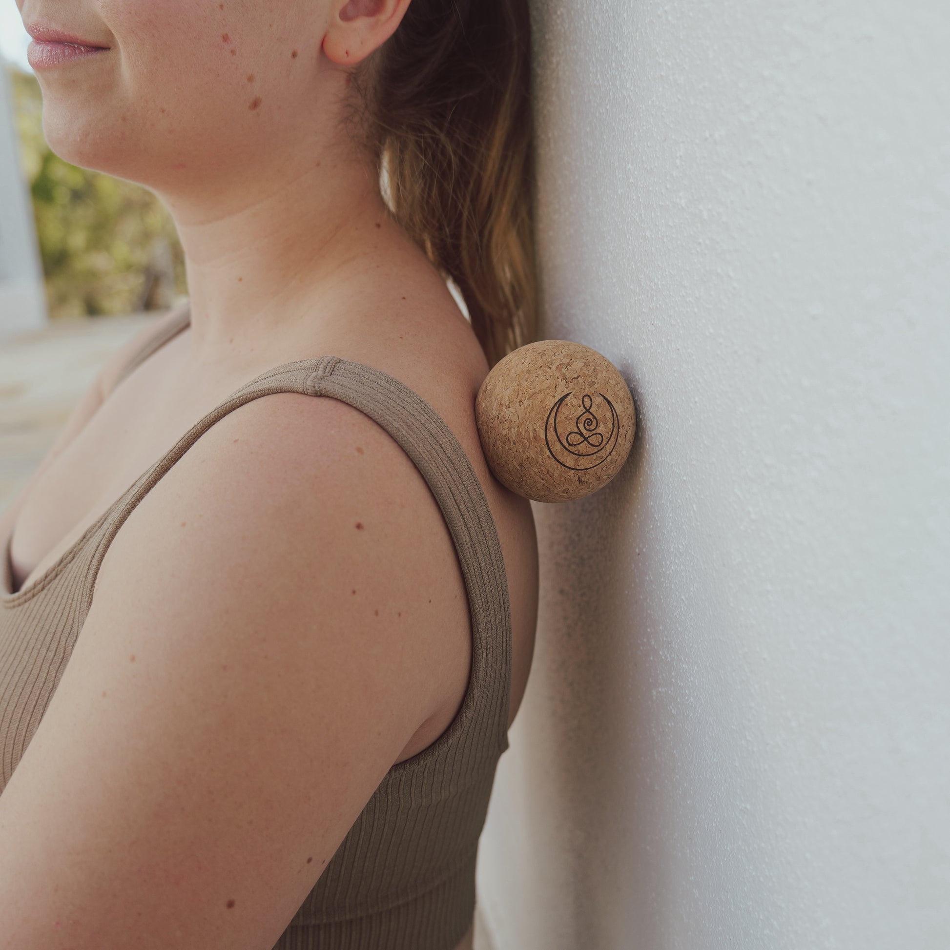 Woman using cork massage balls with OGI NEST logo for back.