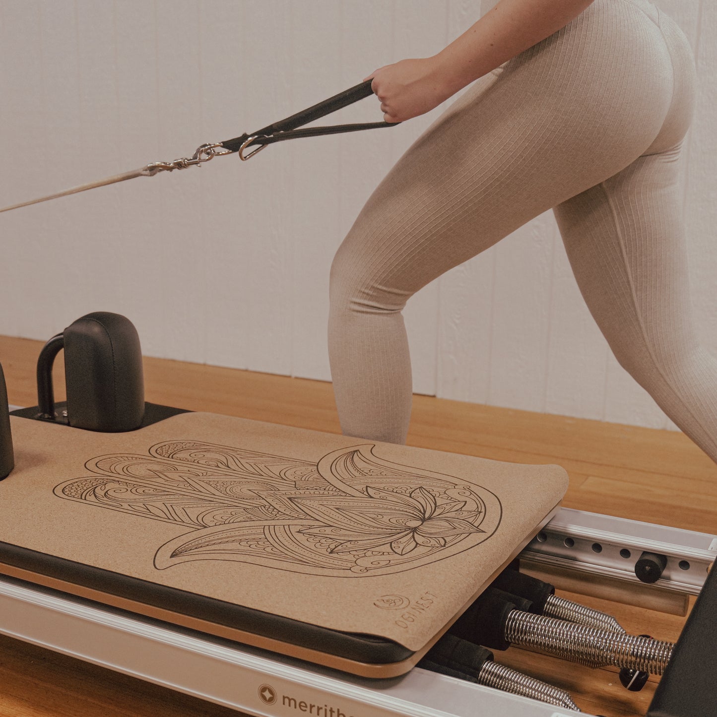 Woman performing single arm cable row next to hamsa hand cork and natural rubber Pilates reformer mat.